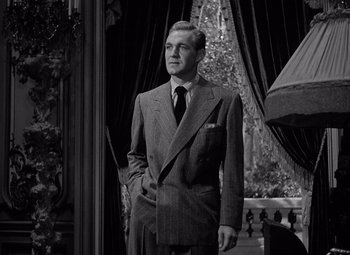 Movie still from “Keeper of the Flame” (1942), directed by George Cukor – A man in a suit and tie standing in front of a window; Medium shot, Low angle