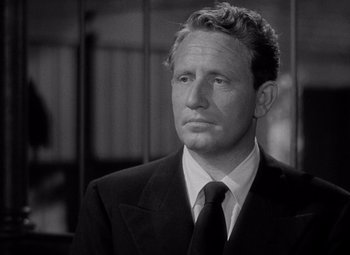 Movie still from “Keeper of the Flame” (1942), directed by George Cukor – A man wearing a suit and tie in front of a cage; Close Up shot, Low angle