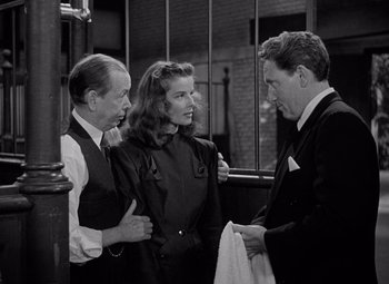 Movie still from “Keeper of the Flame” (1942), directed by George Cukor – Two men and a woman standing next to each other; Medium shot, Over the shoulder angle