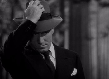 Movie still from “Keeper of the Flame” (1942), directed by George Cukor – A black and white photo of a man in a suit and hat; Close Up shot, High angle