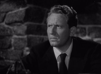 Movie still from “Keeper of the Flame” (1942), directed by George Cukor – A man wearing a suit and tie sitting in front of a brick wall; Close Up shot, High angle