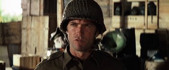 Movie still from “Kelly's Heroes” (1970), directed by Brian G. Hutton – A man wearing a military uniform and a helmet; Close Up shot, Over the shoulder angle