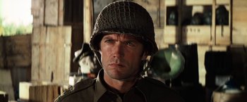 Movie still from “Kelly's Heroes” (1970), directed by Brian G. Hutton – A man wearing a military helmet in a room; Close Up shot, Over the shoulder angle