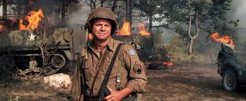Movie still from “Kelly's Heroes” (1970), directed by Brian G. Hutton – A man in a military uniform standing in front of a burning building; Medium shot, Over the shoulder angle
