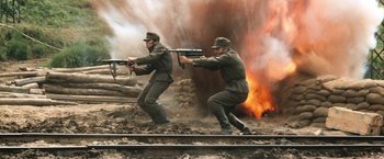 Movie still from “Kelly's Heroes” (1970), directed by Brian G. Hutton – Two men in military uniforms are aiming guns at fire; Wide shot, High angle
