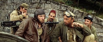Movie still from “Kelly's Heroes” (1970), directed by Brian G. Hutton – A group of men standing next to a stone wall; Medium shot, Over the shoulder angle
