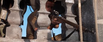 Movie still from “Kelly's Heroes” (1970), directed by Brian G. Hutton – A man holding a gun while standing next to a wall; Medium shot, Low angle