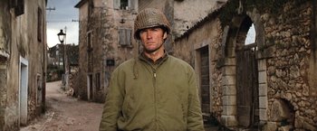 Movie still from “Kelly's Heroes” (1970), directed by Brian G. Hutton – A man wearing a helmet standing in front of a building; Medium shot, Over the shoulder angle