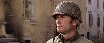Movie still from “Kelly's Heroes” (1970), directed by Brian G. Hutton – A man wearing a helmet in front of a building; Close Up shot, Over the shoulder angle
