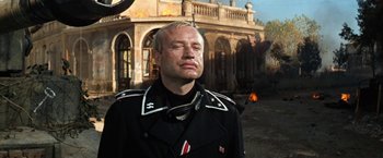 Movie still from “Kelly's Heroes” (1970), directed by Brian G. Hutton – A man in a uniform is standing in front of a building; Medium shot, Low angle