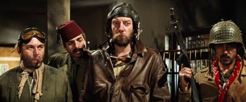 Movie still from “Kelly's Heroes” (1970), directed by Brian G. Hutton – A man in a leather jacket and a hat is smoking a pipe; Medium shot, Low angle