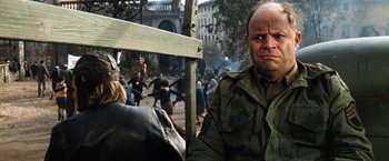 Movie still from “Kelly's Heroes” (1970), directed by Brian G. Hutton – A man in a military jacket is sitting in front of a group of people; Close Up shot, Over the shoulder angle