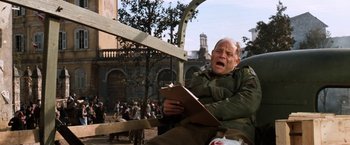 Movie still from “Kelly's Heroes” (1970), directed by Brian G. Hutton – An old man sitting on a bench holding a clipboard; Medium shot, Low angle