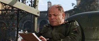 Movie still from “Kelly's Heroes” (1970), directed by Brian G. Hutton – A man sitting in a chair writing on a piece of paper; Close Up shot, High angle