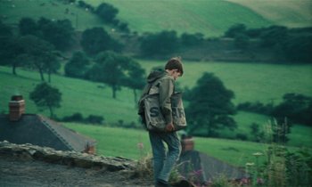 Movie still from “Kes” (1969), directed by Ken Loach – A young man with a backpack walking down a hill; Wide shot, High angle