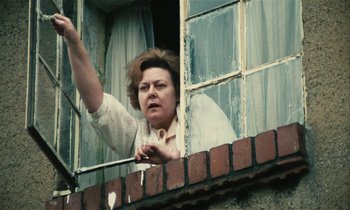 Movie still from “Kes” (1969), directed by Ken Loach – An older woman standing at the window of a house; Medium shot, Low angle