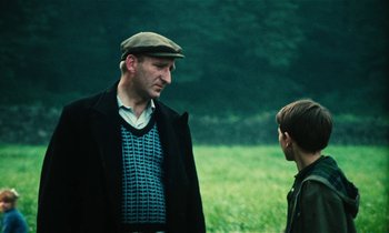 Movie still from “Kes” (1969), directed by Ken Loach – A man and a boy are standing in a field; Medium shot, Over the shoulder angle