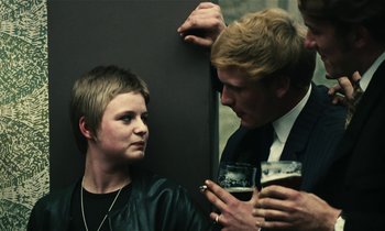 Movie still from “Kes” (1969), directed by Ken Loach – A man and a woman standing next to each other holding beers; Close Up shot, Over the shoulder angle