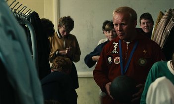 Movie still from “Kes” (1969), directed by Ken Loach – A group of people standing in a room; Medium shot, Over the shoulder angle