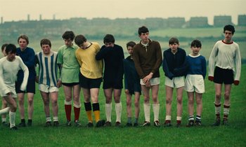 Movie still from “Kes” (1969), directed by Ken Loach – A group of young men standing next to each other on top of a grass field; Wide shot, High angle