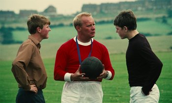 Movie still from “Kes” (1969), directed by Ken Loach – A group of young men standing next to each other holding a soccer ball; Medium shot, Over the shoulder angle
