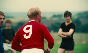 Movie still from “Kes” (1969), directed by Ken Loach – Two men are playing soccer on a field; Medium shot, Over the shoulder angle