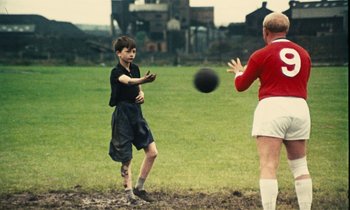 Movie still from “Kes” (1969), directed by Ken Loach – Two young men playing a game of soccer on a field; Wide shot, High angle