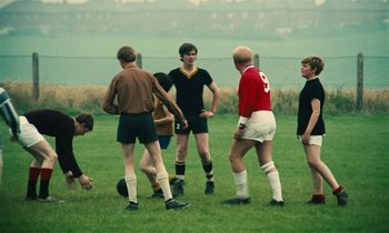 Movie still from “Kes” (1969), directed by Ken Loach – A group of young men standing on top of a soccer field; Wide shot, High angle