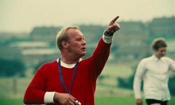 Movie still from “Kes” (1969), directed by Ken Loach – A man in a red shirt is pointing to the sky; Medium shot, Over the shoulder angle