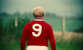 Movie still from “Kes” (1969), directed by Ken Loach – A man in a red and white soccer uniform; Medium shot, Over the shoulder angle