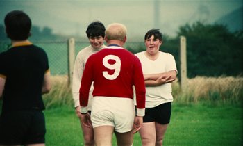 Movie still from “Kes” (1969), directed by Ken Loach – A group of young men standing on top of a grass covered field; Medium shot, Over the shoulder angle