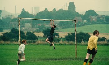 Movie still from “Kes” (1969), directed by Ken Loach – A young man hanging from a bar in a field; Wide shot, Low angle