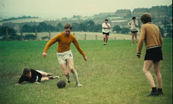 Movie still from “Kes” (1969), directed by Ken Loach – A group of men playing a game of soccer on a grassy field; Wide shot, High angle