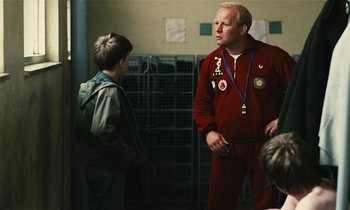 Movie still from “Kes” (1969), directed by Ken Loach – A man in a red jacket talking to a boy in a green jacket; Medium shot, Over the shoulder angle