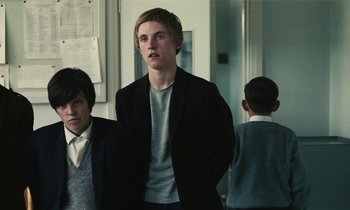 Movie still from “Kes” (1969), directed by Ken Loach – Two young men standing next to each other in front of a wall; Medium shot, Low angle