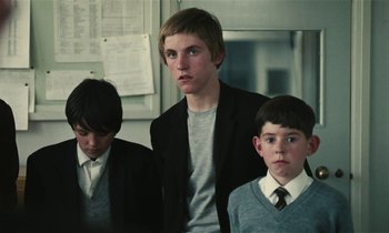 Movie still from “Kes” (1969), directed by Ken Loach – Three young men standing next to each other in a room; Medium shot, Over the shoulder angle