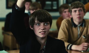 Movie still from “Kes” (1969), directed by Ken Loach – A young man is sitting in front of a group of other young men; Close Up shot, Over the shoulder angle