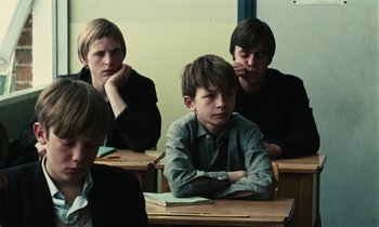 Movie still from “Kes” (1969), directed by Ken Loach – A group of young men sitting at a desk; Medium shot, High angle