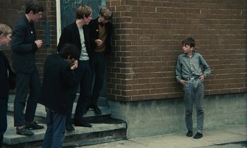 Movie still from “Kes” (1969), directed by Ken Loach – A group of young men standing next to a brick wall; Wide shot, High angle