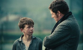 Movie still from “Kes” (1969), directed by Ken Loach – A man standing next to a young boy in a field; Medium shot, Over the shoulder angle
