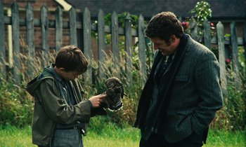Movie still from “Kes” (1969), directed by Ken Loach – A man and a boy looking at an owl in the grass; Medium shot, Over the shoulder angle