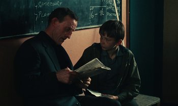 Movie still from “Kes” (1969), directed by Ken Loach – A man sitting next to another man holding a newspaper; Medium shot, Over the shoulder angle