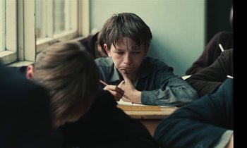 Movie still from “Kes” (1969), directed by Ken Loach – A young boy sitting at a table with his hand under his chin; Close Up shot, Over the shoulder angle
