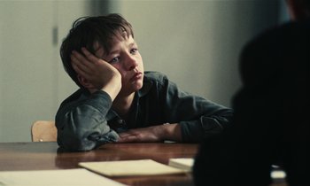 Movie still from “Kes” (1969), directed by Ken Loach – A boy sitting at a table with his head resting on his hand; Close Up shot, Over the shoulder angle