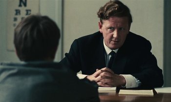 Movie still from “Kes” (1969), directed by Ken Loach – A man sitting at a table talking to another man; Close Up shot, Over the shoulder angle