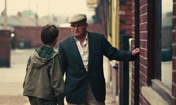 Movie still from “Kes” (1969), directed by Ken Loach – An older man and a young boy are walking down the street; Medium shot, Over the shoulder angle