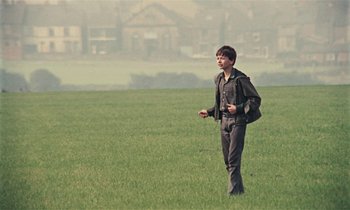 Movie still from “Kes” (1969), directed by Ken Loach – A young boy in a field with a backpack; Wide shot, High angle