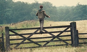 Movie still from “Kes” (1969), directed by Ken Loach – A boy standing on top of a wooden fence; Wide shot, Low angle