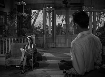 Movie still from “Key Largo” (1948), directed by John Huston – A man sitting on a chair reading a newspaper; Wide shot, Over the shoulder angle