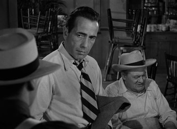 Movie still from “Key Largo” (1948), directed by John Huston – A black and white photo of a man wearing a tie; Medium shot, Over the shoulder angle